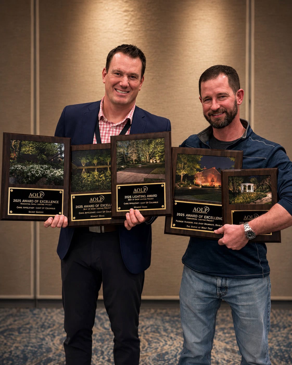 Two men stand side by side indoors, each holding multiple award plaques featuring nature photos and the text “AOLP Award of Excellence” for 2023. - Christopher A. Lighting Design